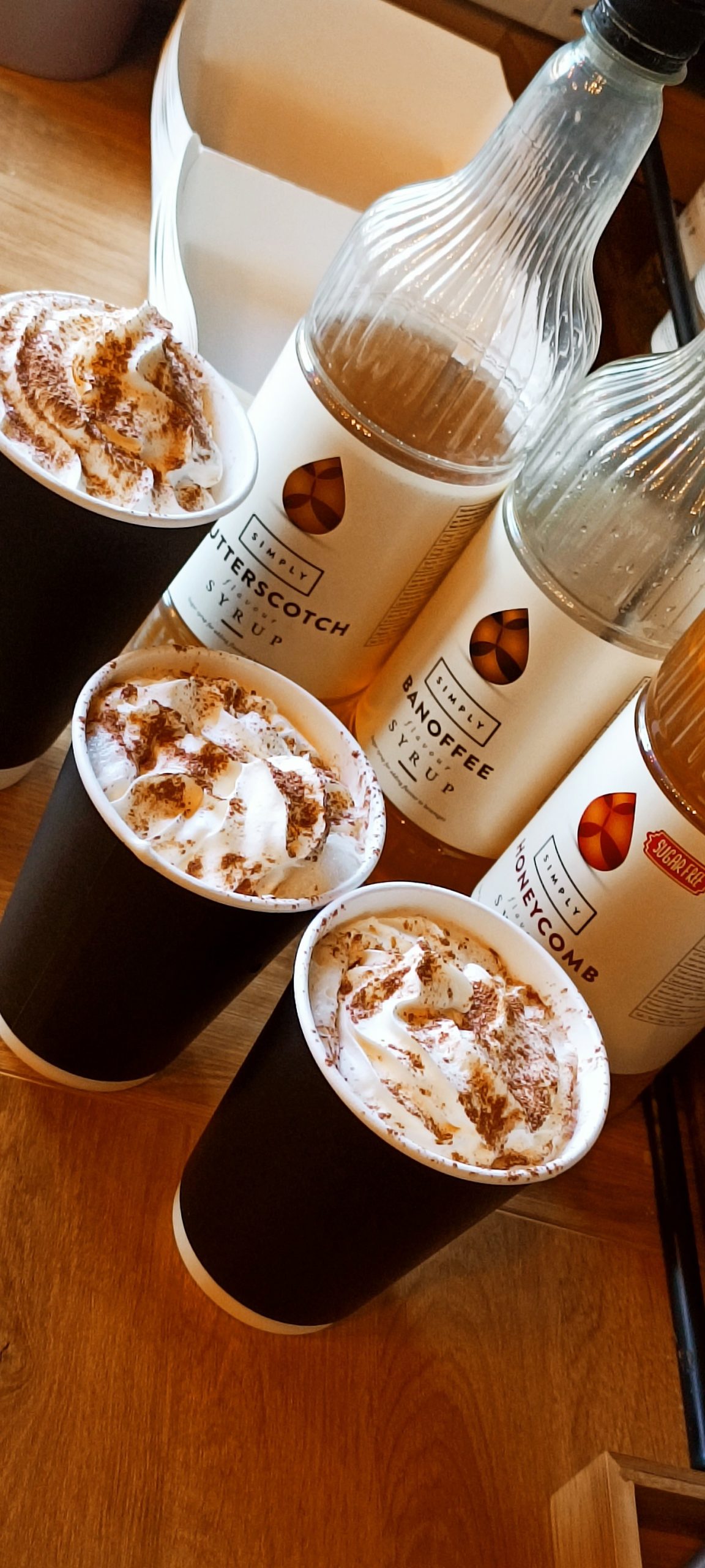 Hot drinks topped with cream beside a selection of flavour syrups
